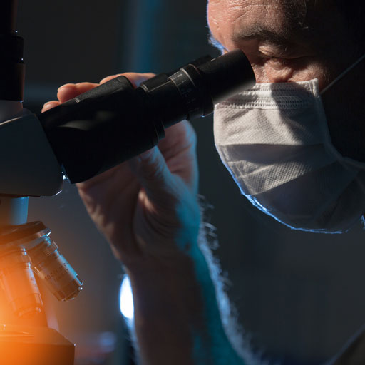 A pathologist in a facemark looks through a microscope